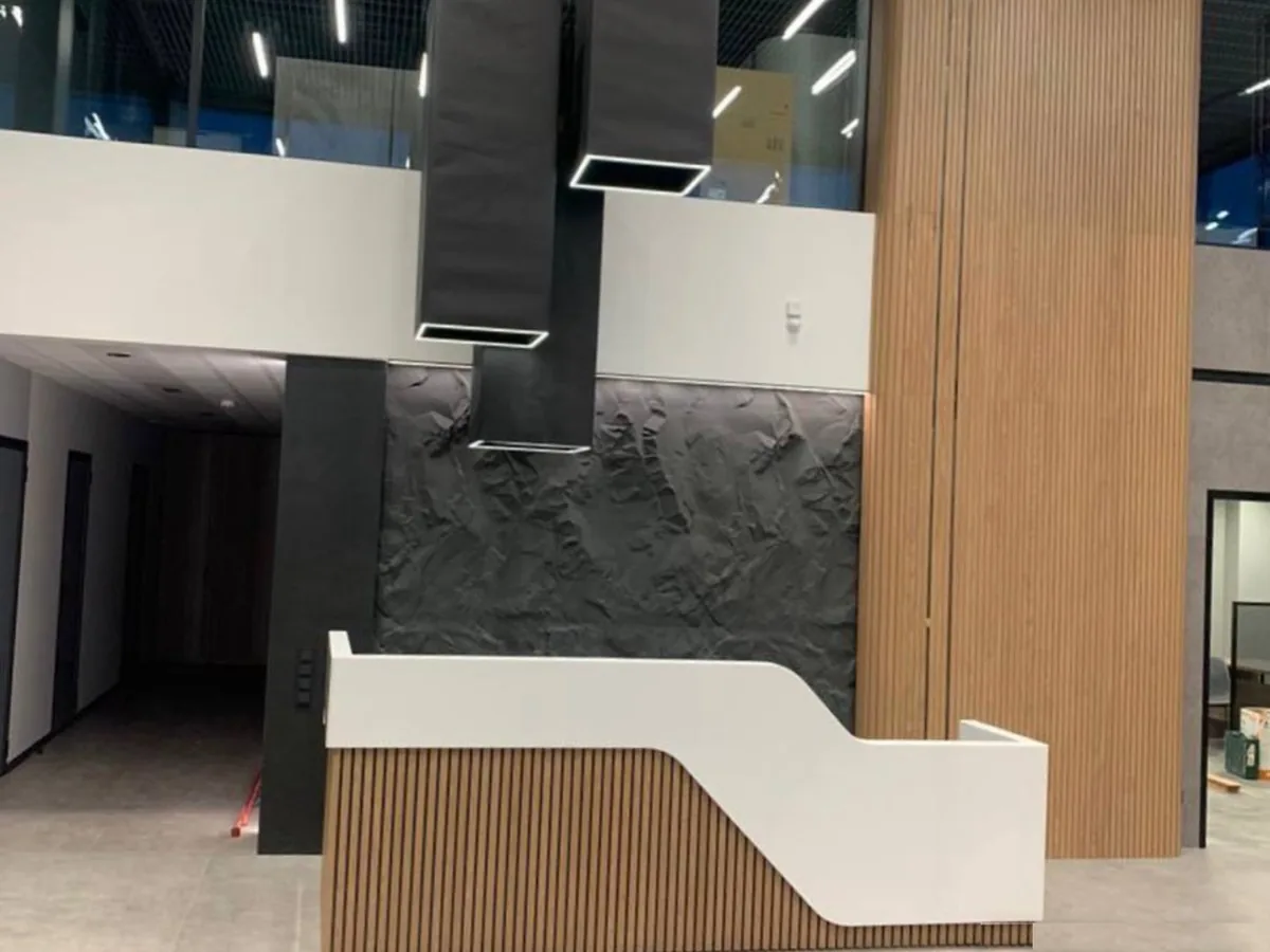 Two-level reception desk in an office lobby: stepped white top and wood-tone slats